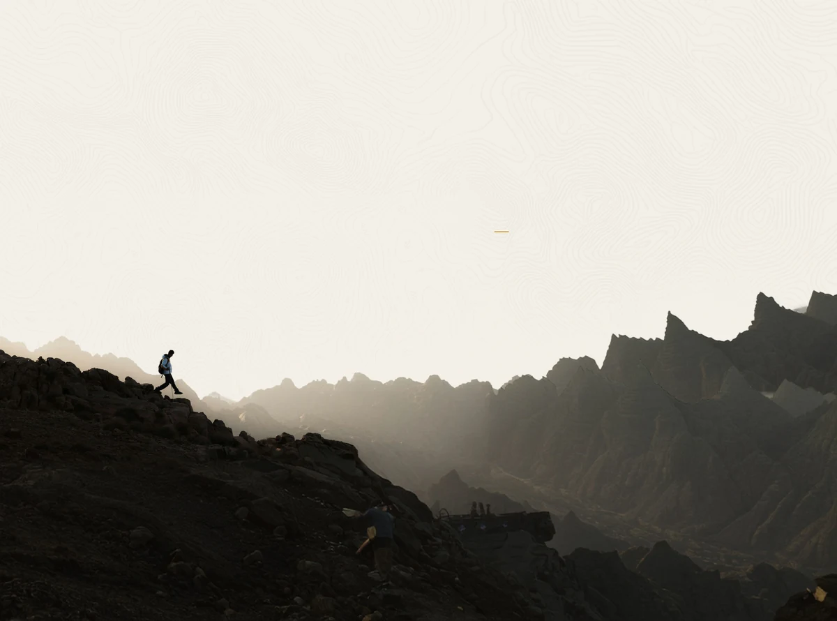 A lone hiker crossing a dark mountain ridge beneath a pale, misted sky